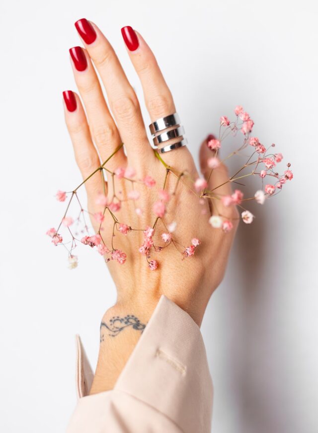 soft-gentle-photo-woman-hand-with-big-ring-red-manicure-hold-cute-little-pink-dried-flowers-white